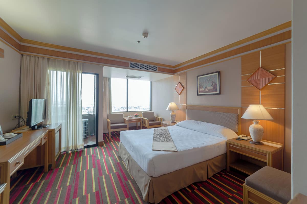 Una habitación de hotel con una cama grande, un escritorio con ordenador, una silla, una mesita con lámpara y una ventana con cortinas.