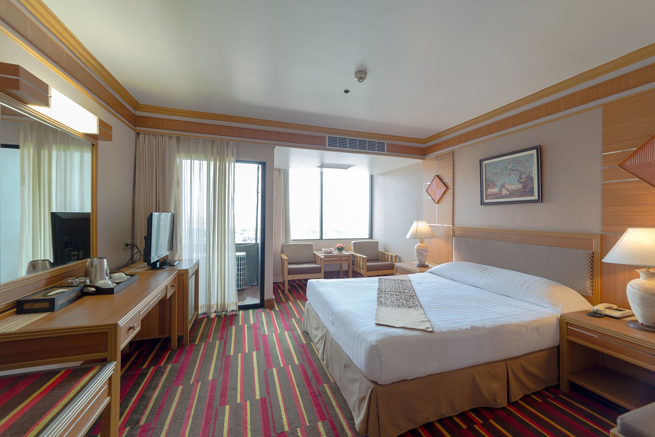 A hotel room with a large bed, a desk with a computer, a chair, a television, and a window with curtains.