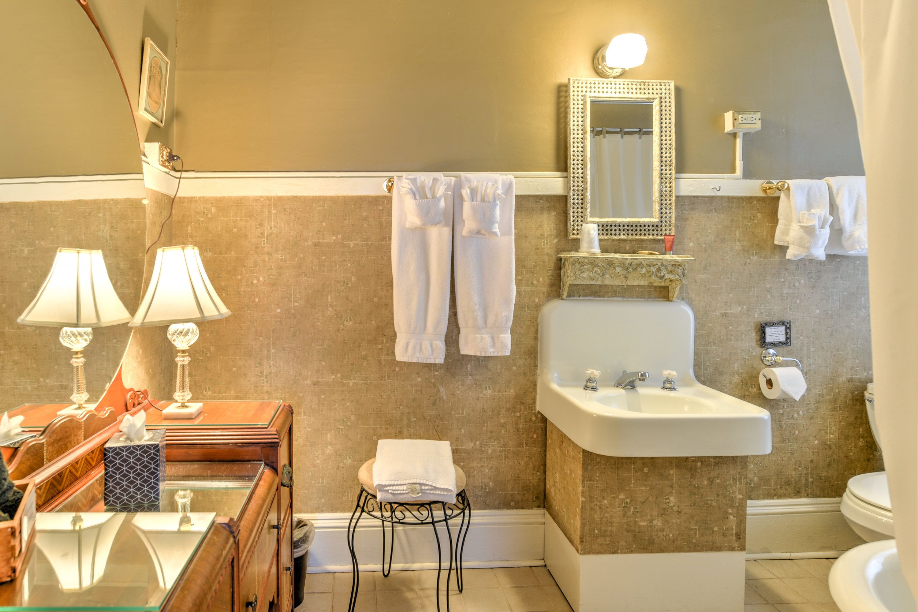 A bathroom with a sink, mirror, towel rack, and a glass-enclosed vanity.