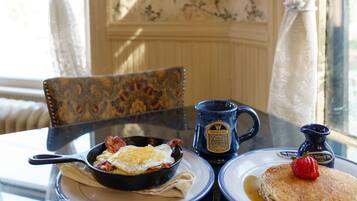 A breakfast table with scrambled eggs, bacon, pancakes, and a muffin, along with a coffee mug and a fruit bowl.