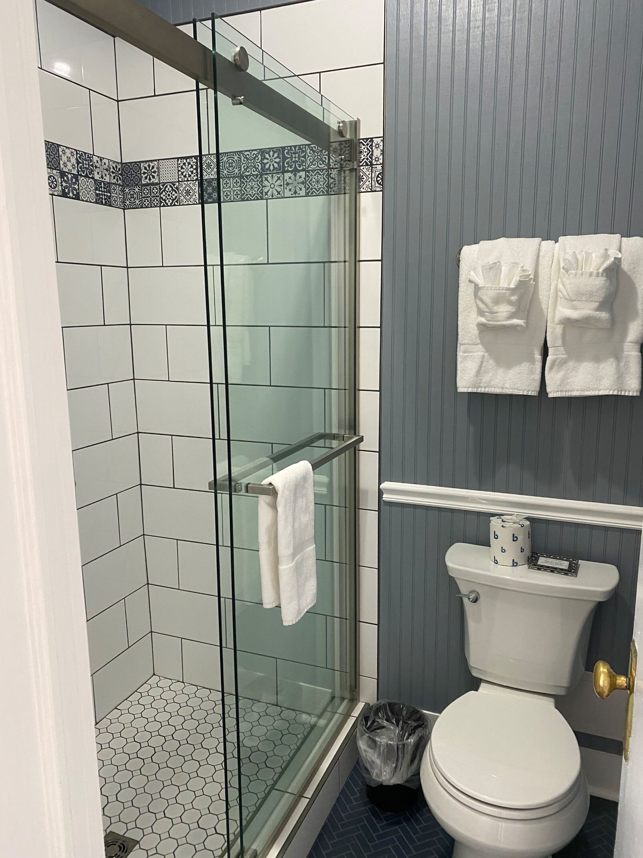 A bathroom with a glass shower enclosure, a toilet, and a trash bin.