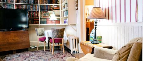 A cozy living room with a large bookshelf, a television, a patterned rug, and a comfortable sofa.