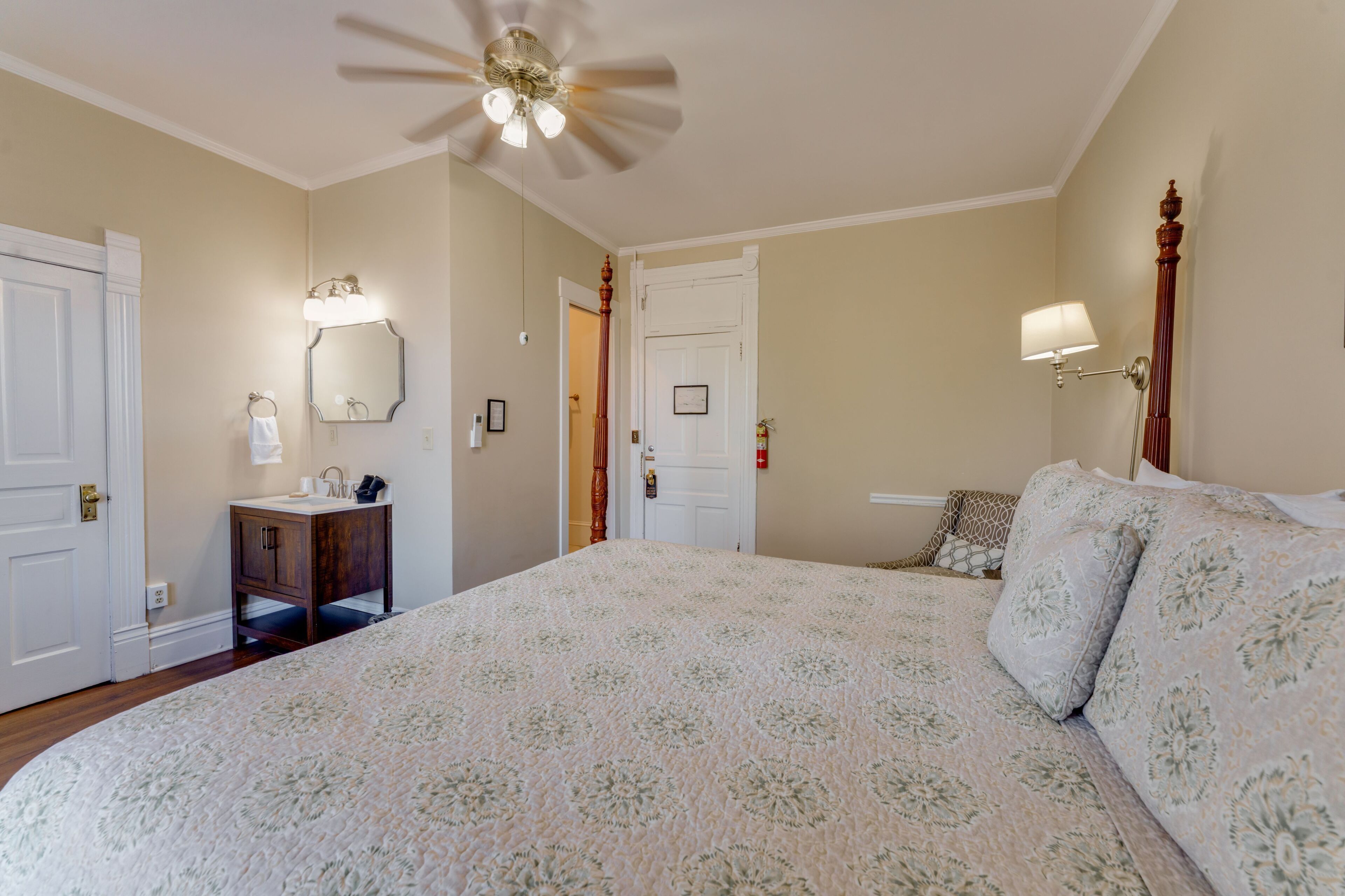 A bedroom with a bed, a nightstand, a mirror, a ceiling fan, and a door.