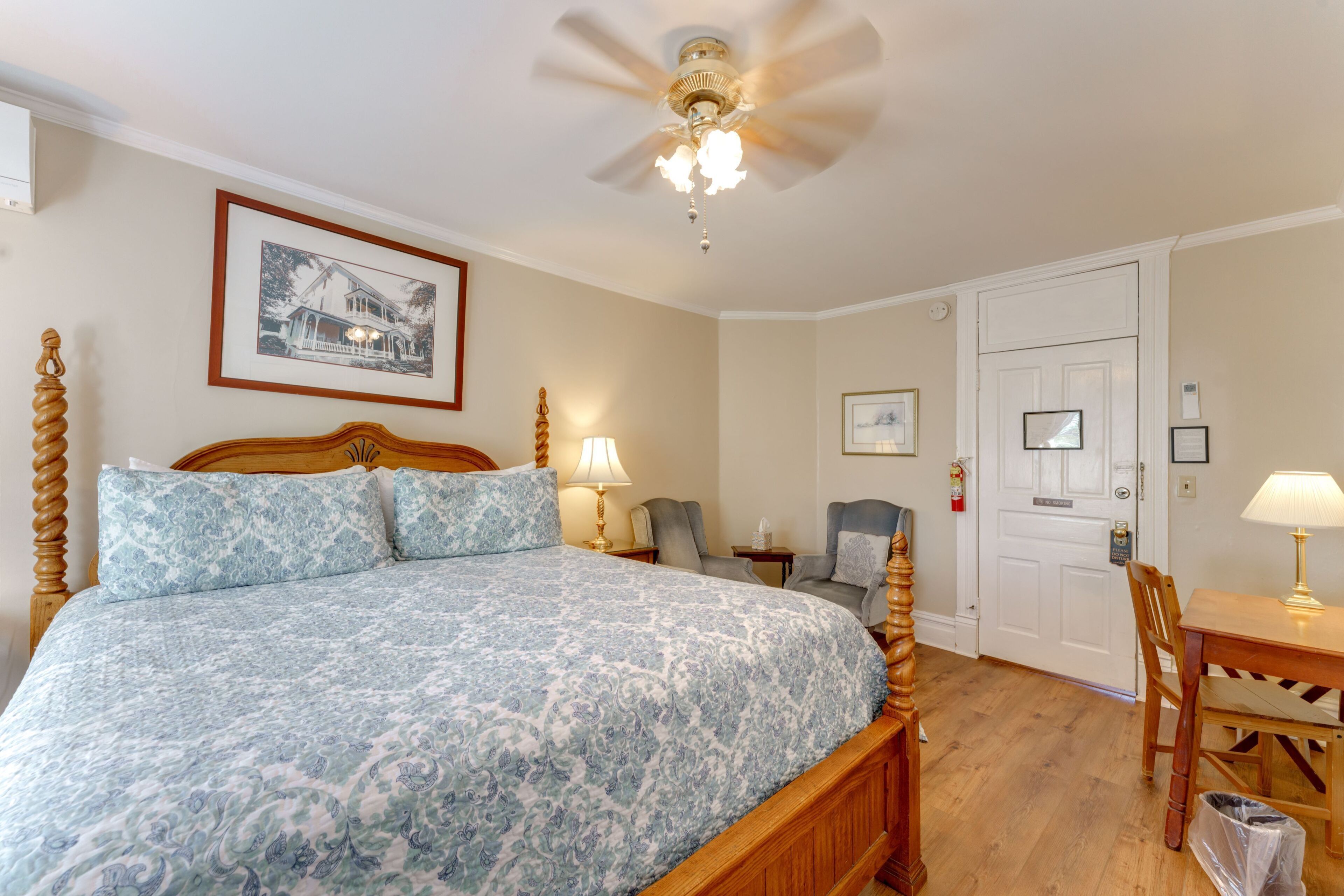 A bedroom with a bed, a ceiling fan, a door, a chair, and a table.