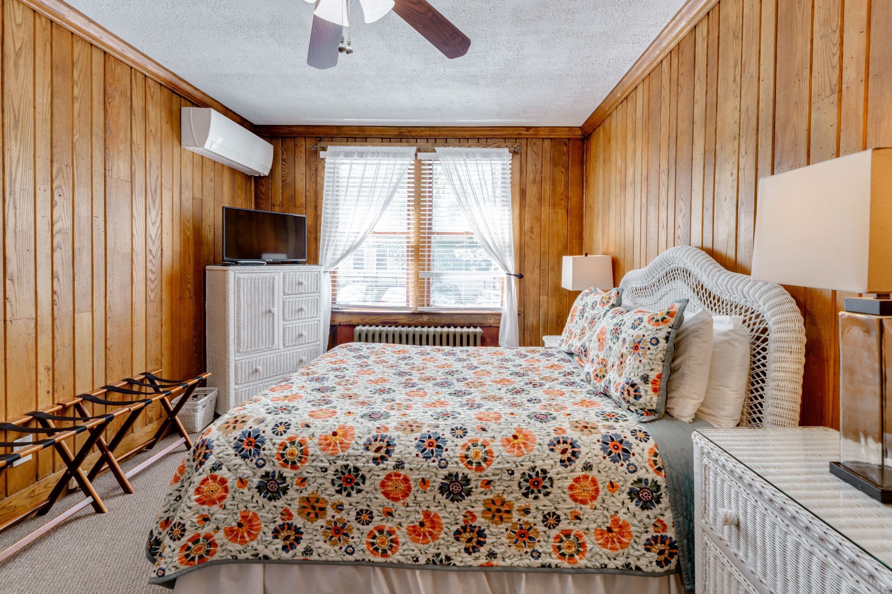 A bedroom with a bed, a television, a radiator, and a window with blinds.