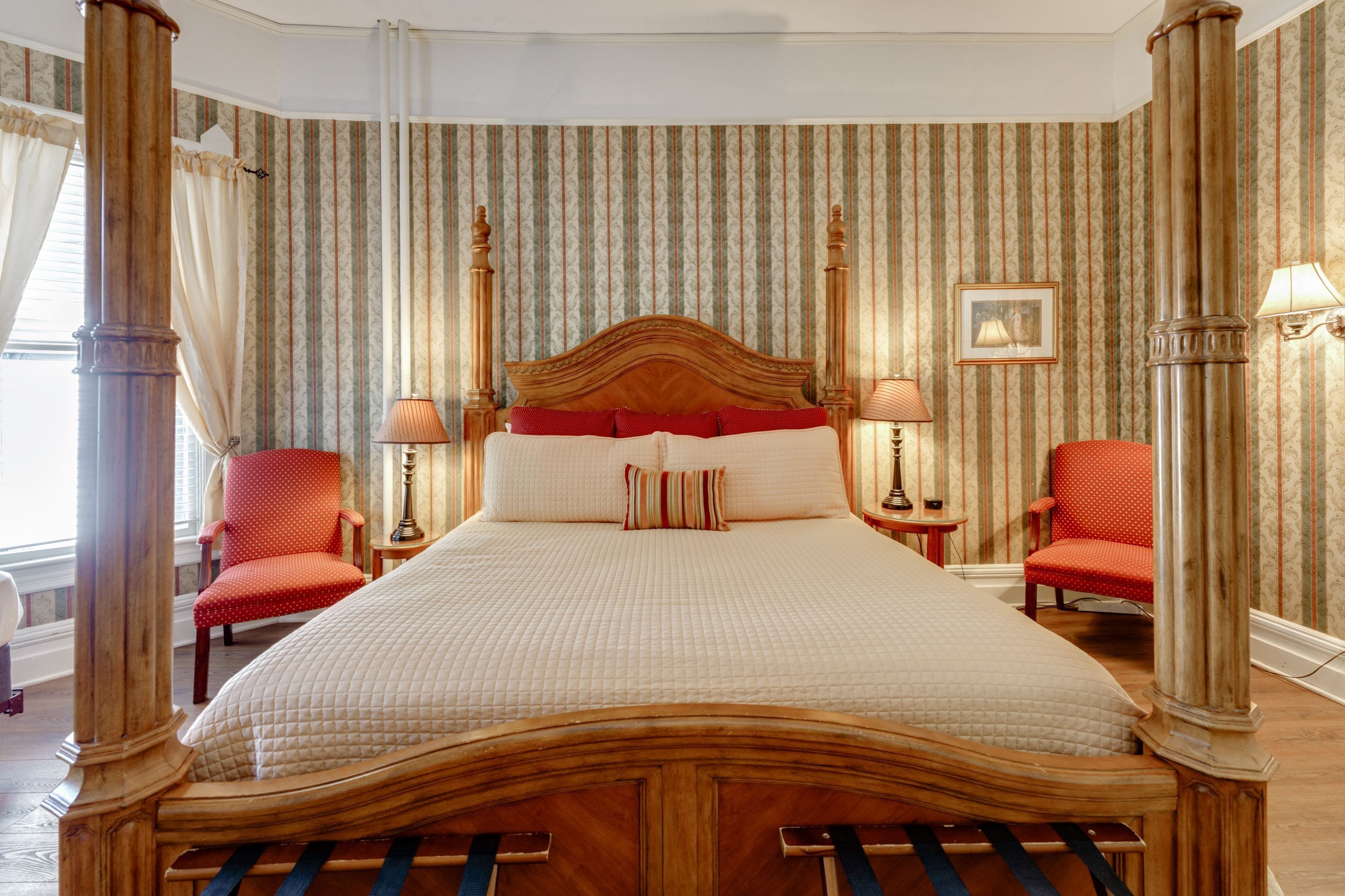 A hotel room with a large bed, two chairs, a nightstand, and a picture on the wall.
