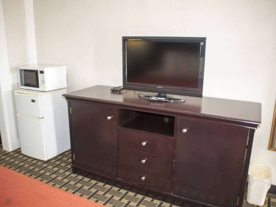 Quarto de hotel com cômoda de madeira escura, TV de tela plana, micro-ondas e geladeira.
