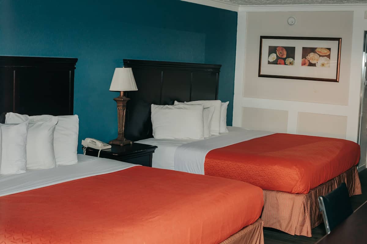 A hotel room with two beds, a nightstand with a lamp, and a framed picture on the wall.