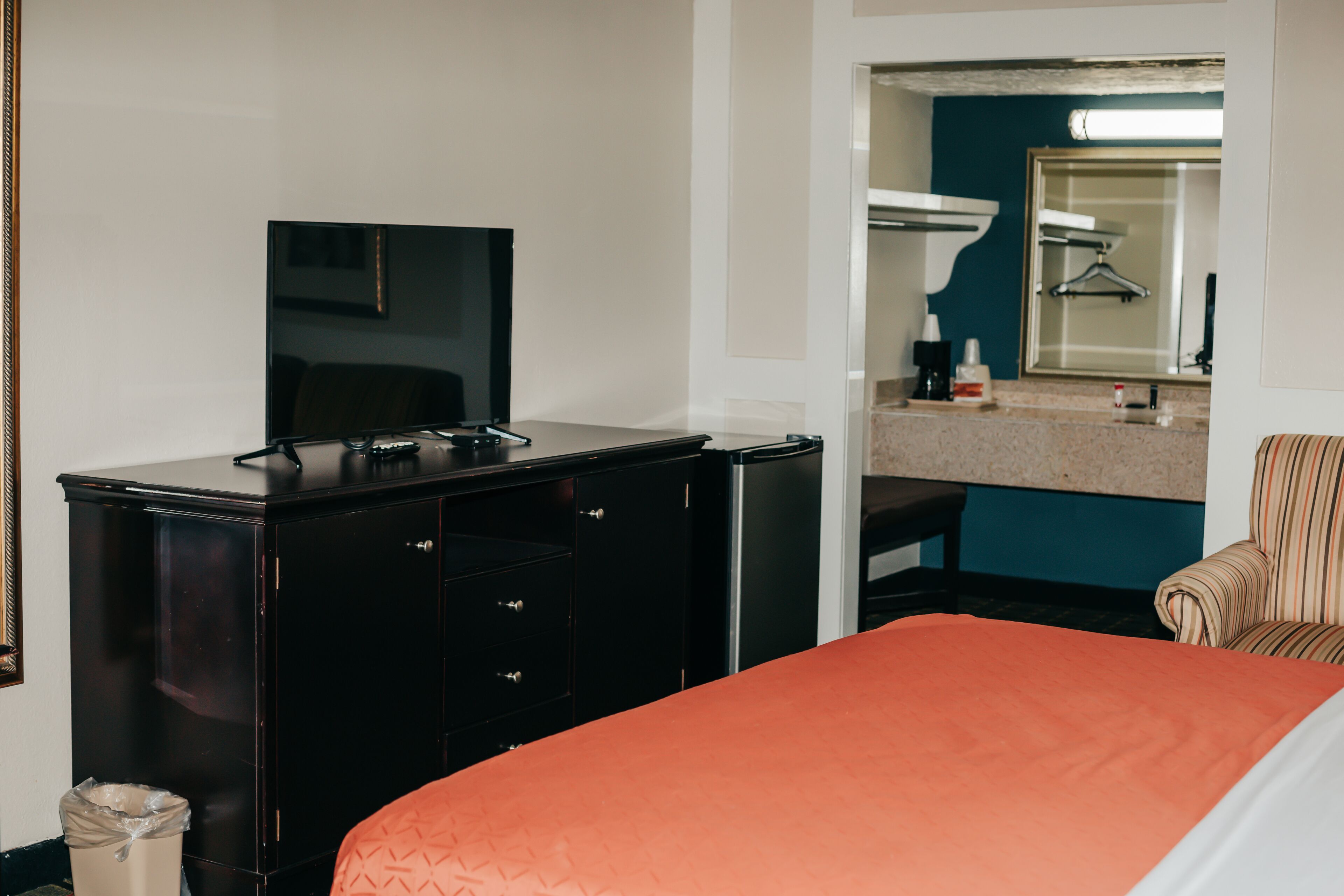 A hotel room with a bed, a TV on a dresser, a mirror, and a bathroom visible through an open door.