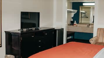 Une chambre d’hôtel avec un lit, un téléviseur posé sur une commode, un miroir et une salle de bain visible à travers une porte ouverte.