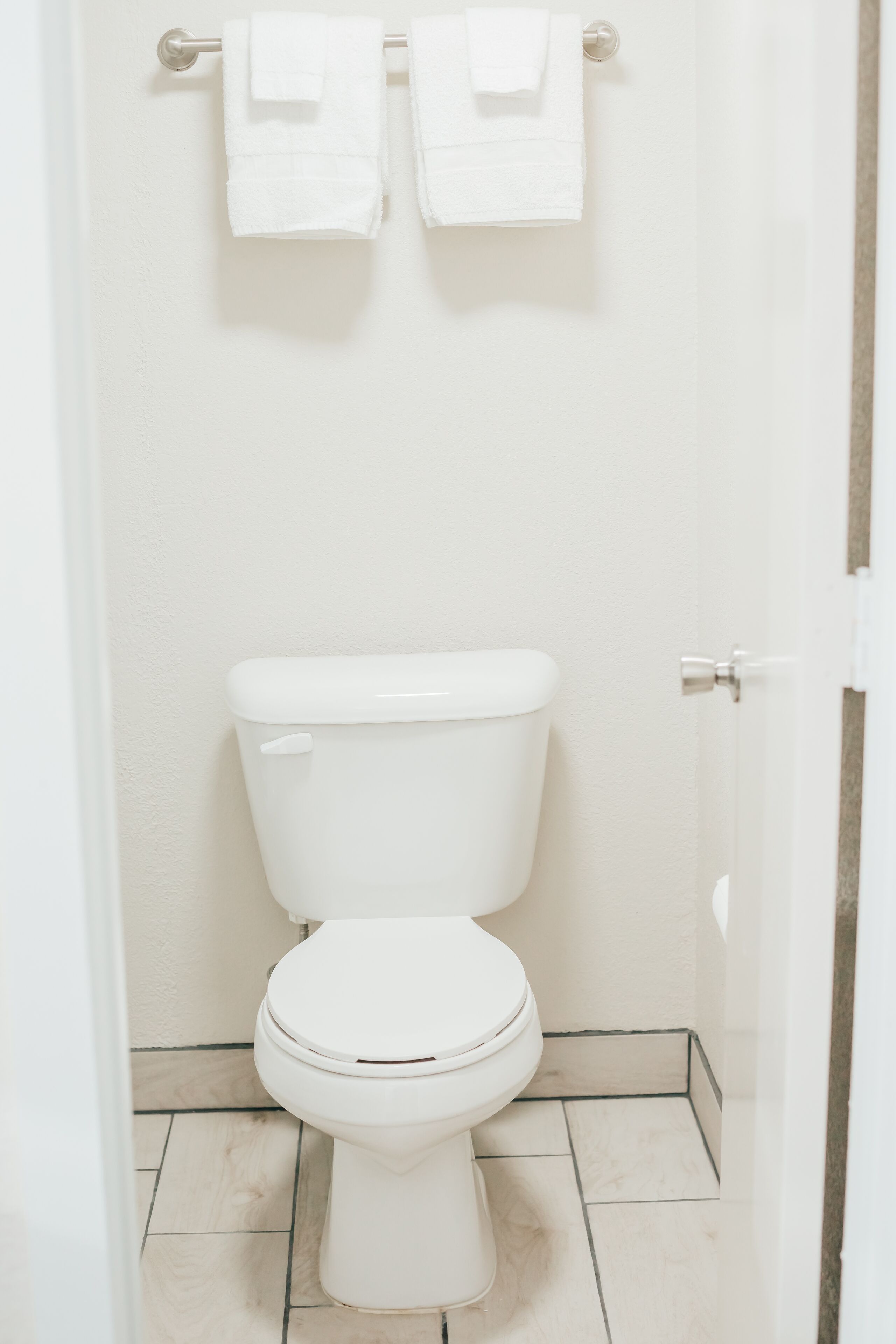 A white toilet with a closed lid, a towel rack with two white towels, and a tiled floor.