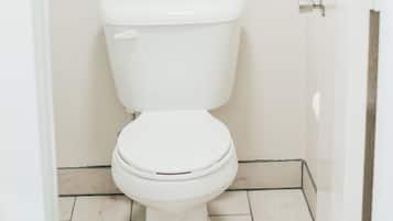 A white toilet with a closed lid, a towel rack with two white towels, and a tiled floor.