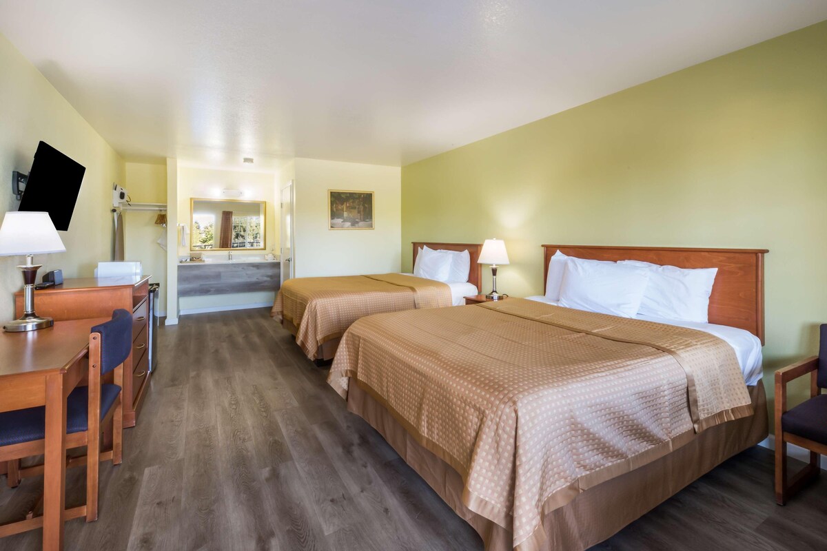 A hotel room with two beds, a desk, chairs, a TV, and a bathroom.