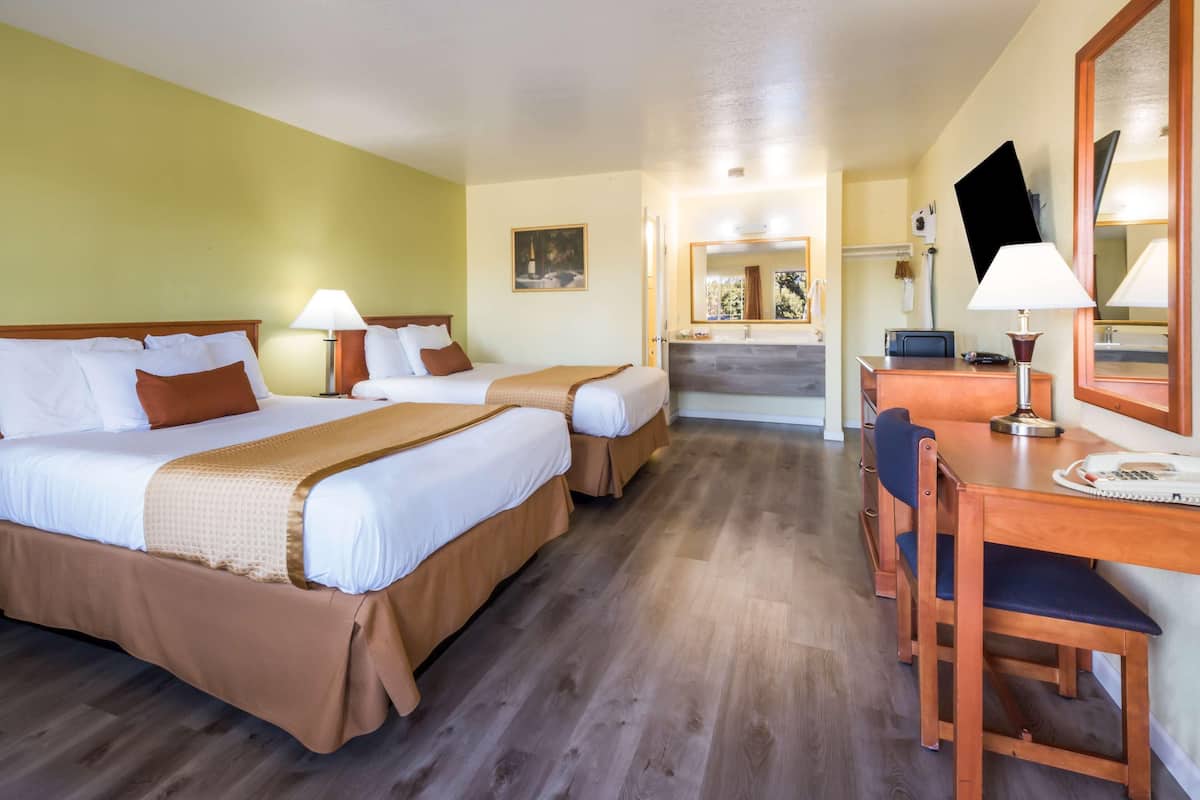A hotel room with two beds, a desk, a chair, a mirror, and a bathroom visible in the background.