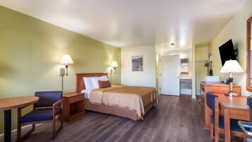 A hotel room with a bed, a desk, a chair, and a lamp.