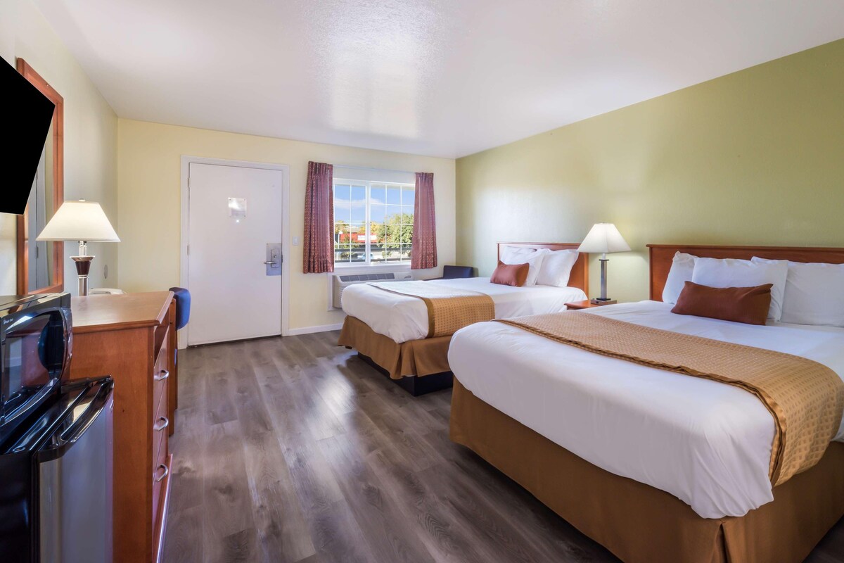 A hotel room with two beds, a desk with a lamp, a television, and a window with curtains.