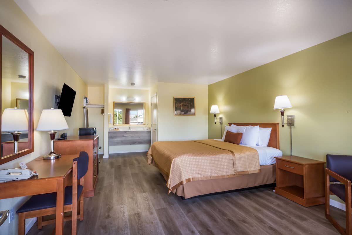 A hotel room with a bed, desk, chair, and a mirror.