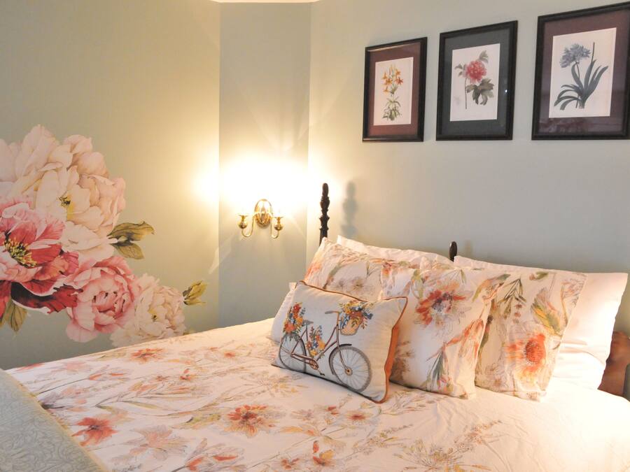A bedroom with a floral bedspread, a bicycle-themed pillow, and three framed floral pictures on the wall.