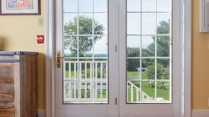 A room with a wooden bench, a white door with glass panels, and a view of a white fence and greenery outside. - Strong House Inn (Vergennes)
