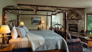 A rustic bedroom with a four-poster bed, a stone fireplace, and a view of the outdoors. - Strong House Inn (Vergennes)