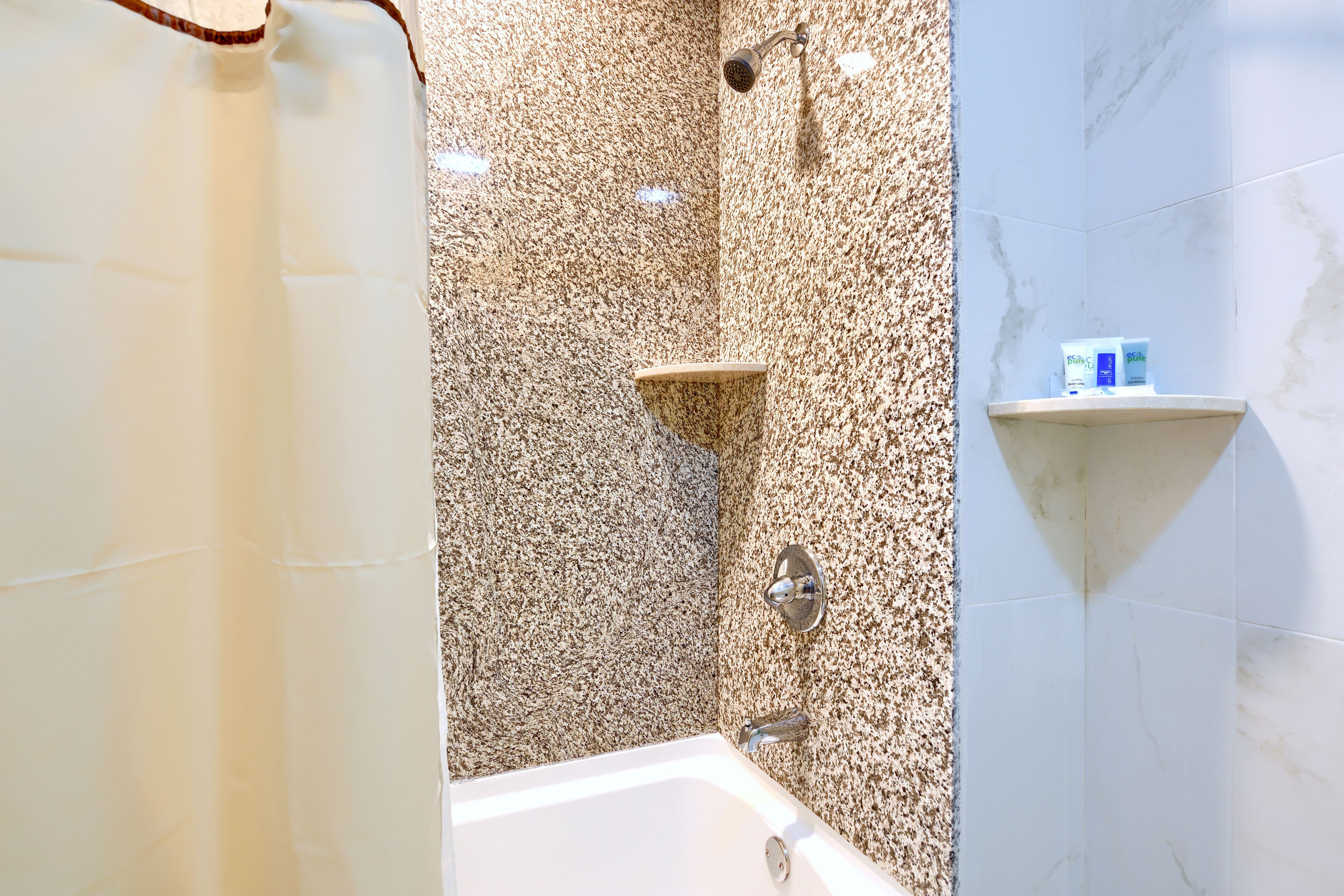 A bathroom with a bathtub, a shower, and a shelf with toiletries.