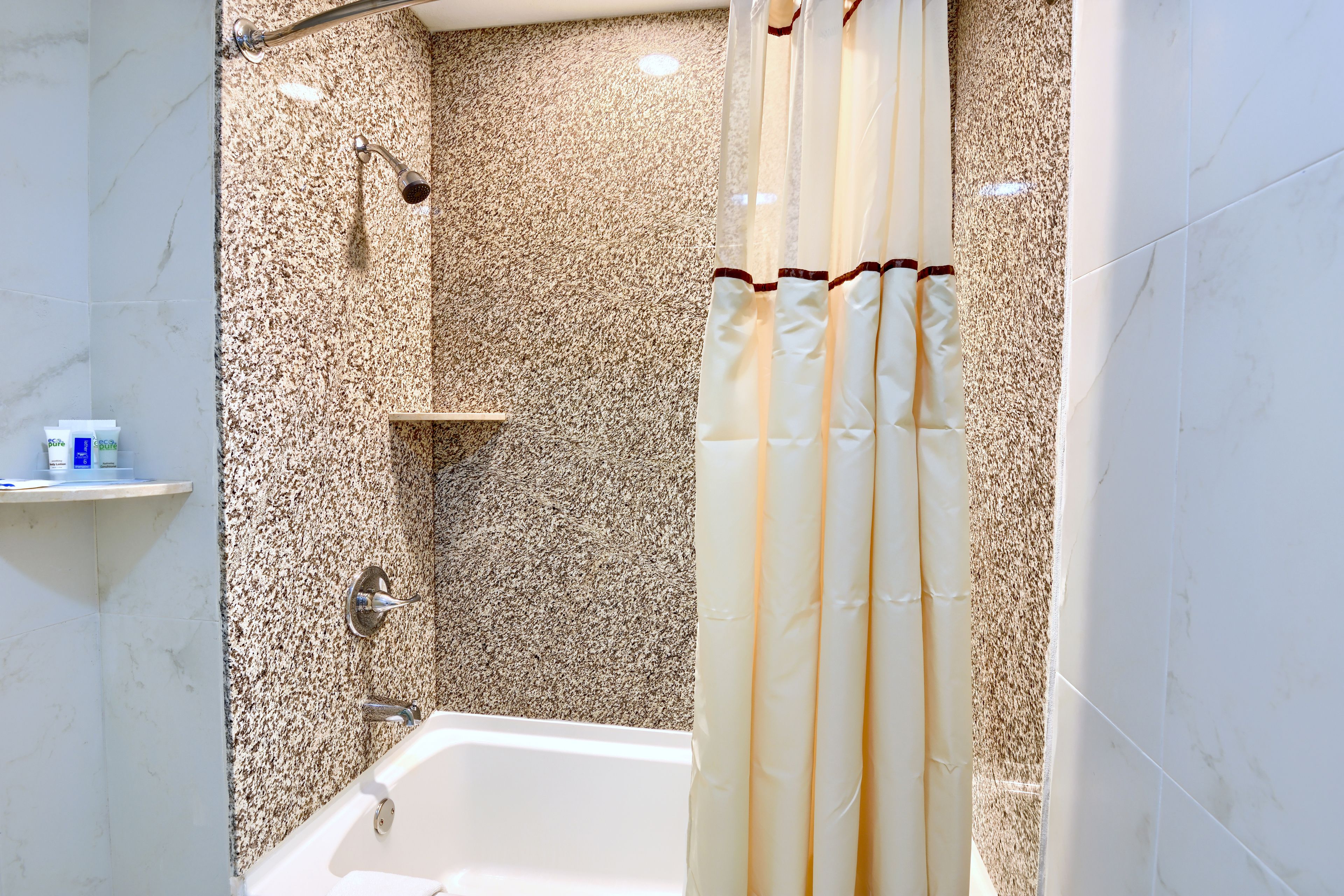 A bathroom with a bathtub, a shower with a glass door, and a marble wall.
