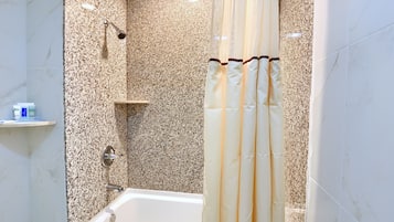 A bathroom with a bathtub, a shower with a glass door, and a marble wall.
