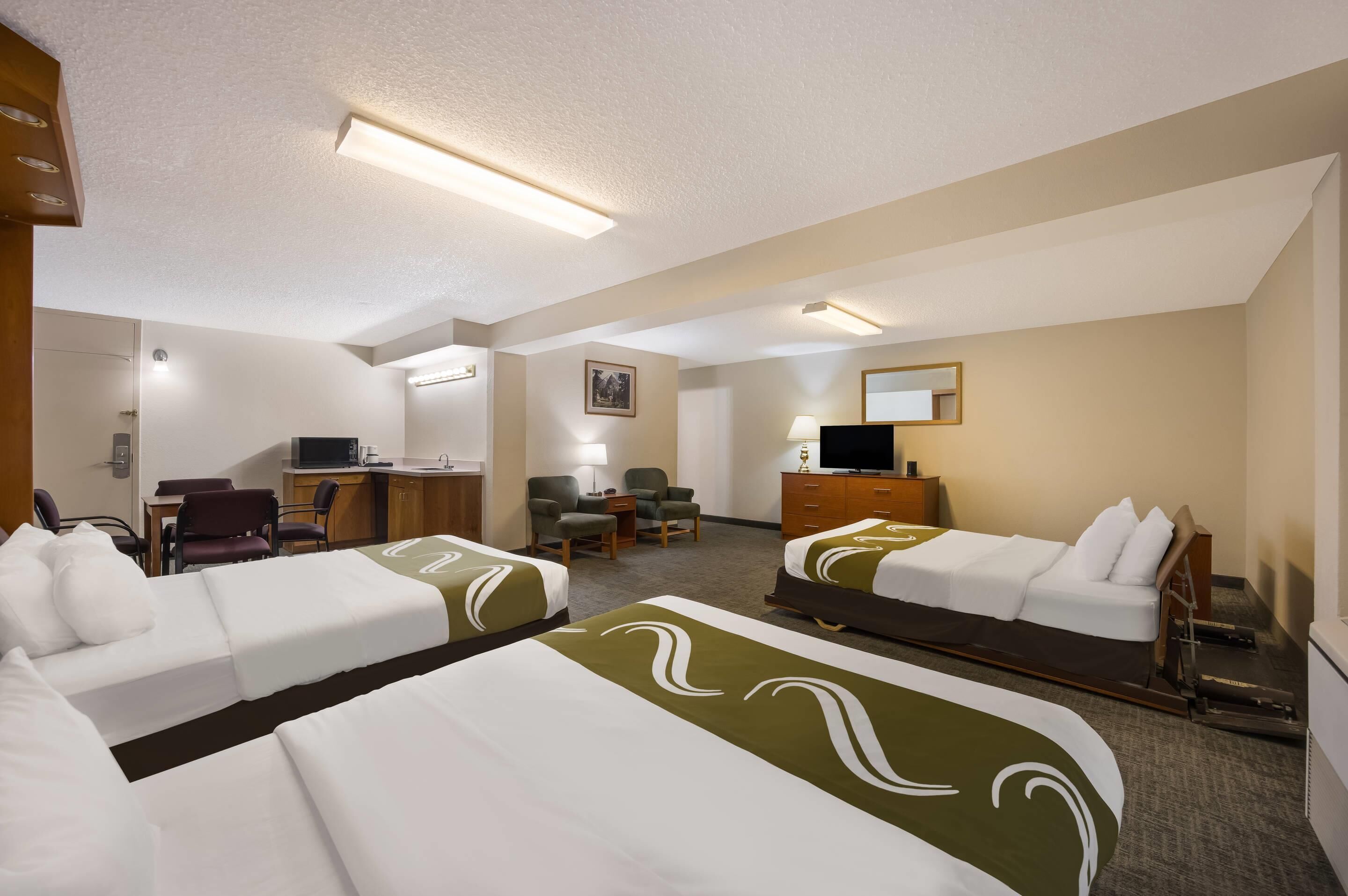 A hotel room with two beds, a desk, a chair, a TV, and a small table with a lamp.