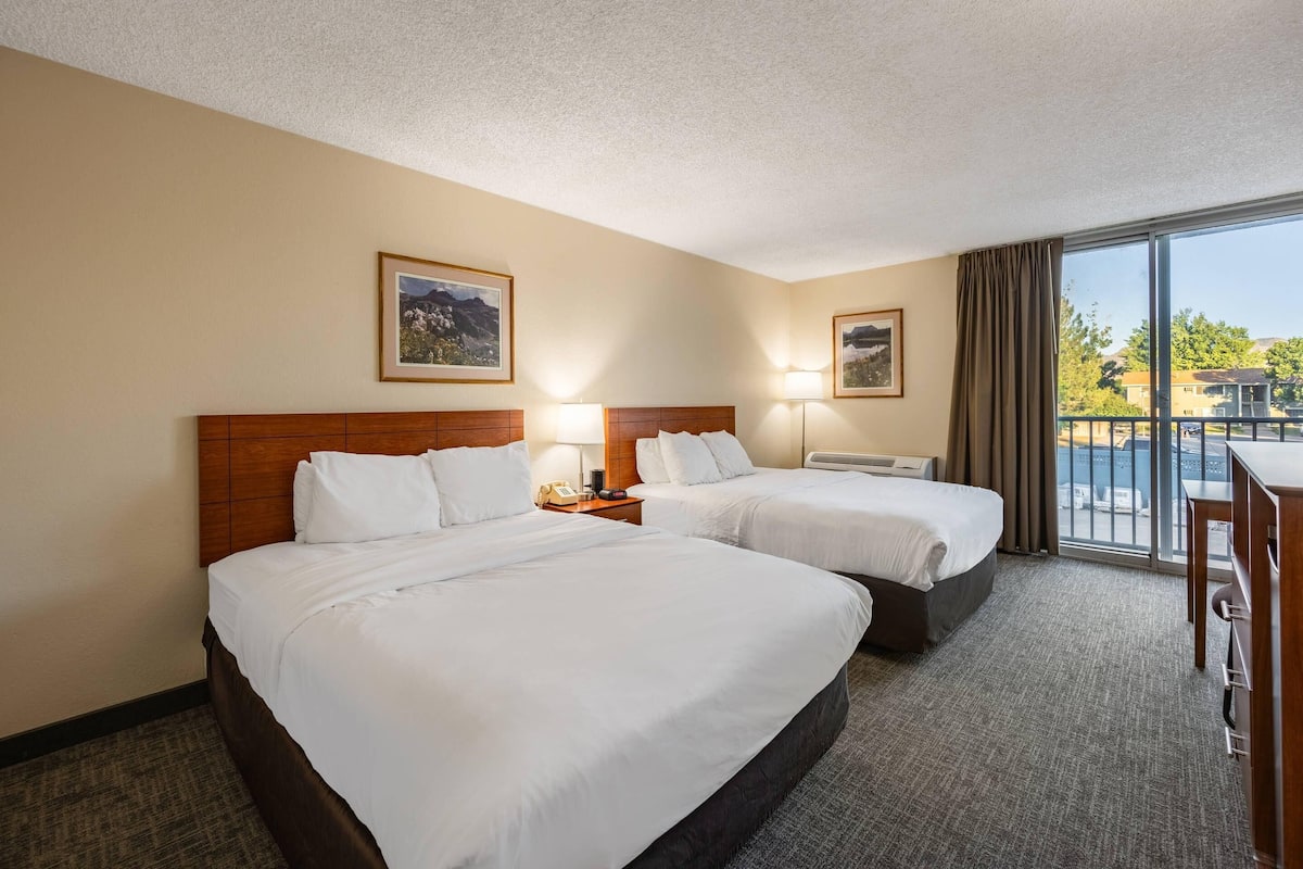 A hotel room with two beds, a large window with a view, and a desk with a chair.