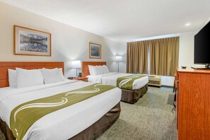 A hotel room with two beds, a wooden headboard, a flat-screen TV, a desk, and a window with curtains.