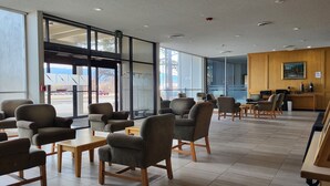 A modern indoor seating area with tables and chairs, large windows, and a reception desk. - Quality Inn & Suites Canon City (Canon City)