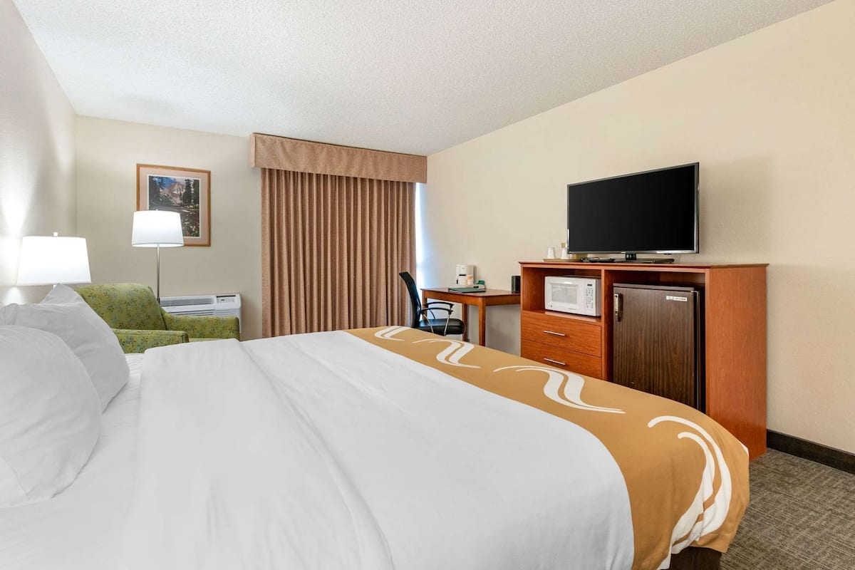 A hotel room with a bed, a desk with a television, a microwave, and a refrigerator.