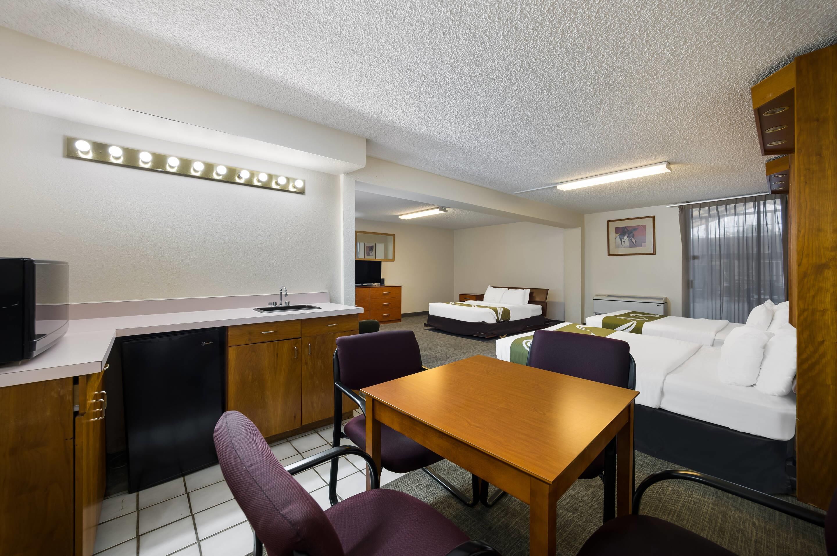 A hotel room with a kitchenette, a dining area, a bed, and a sofa.