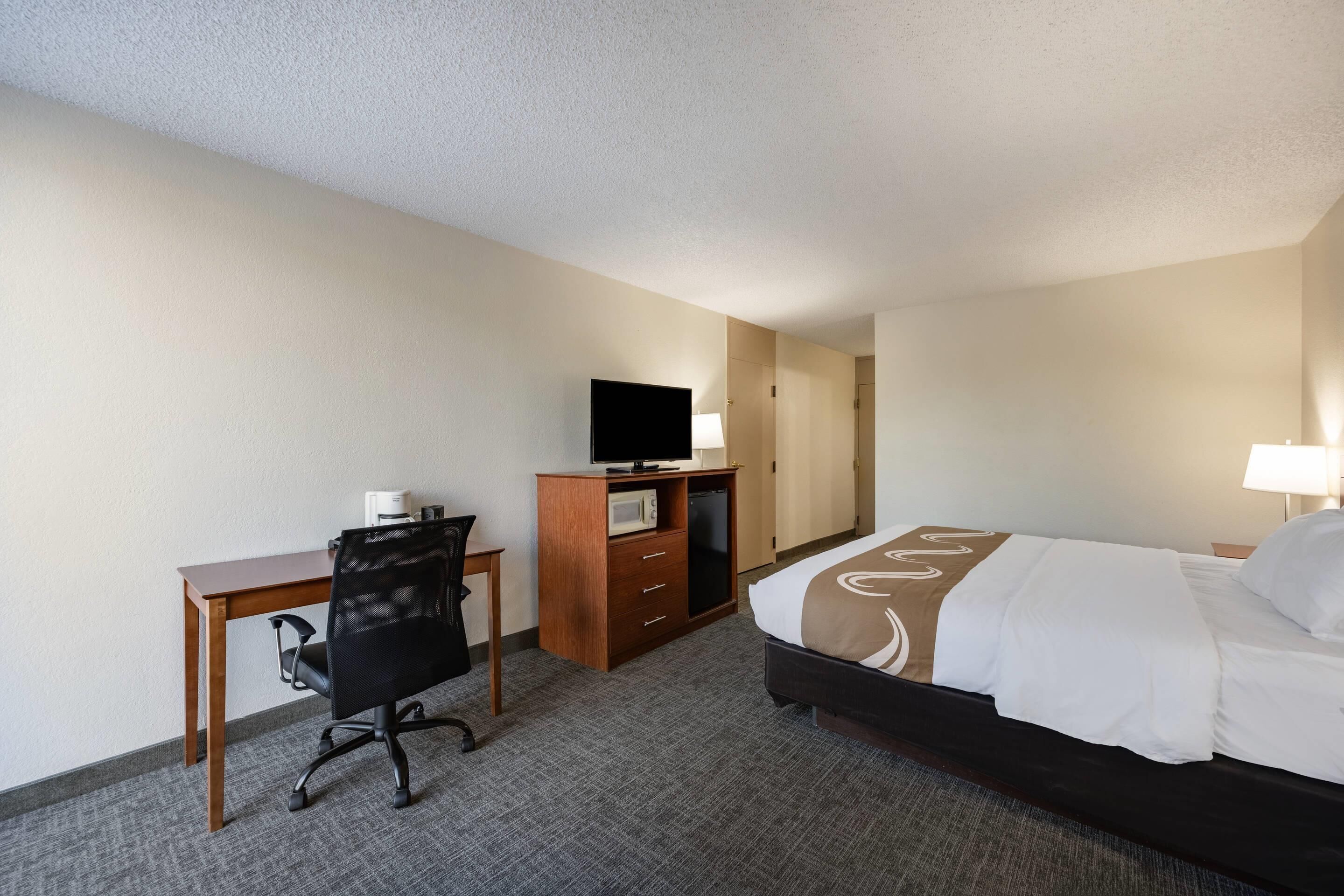 Habitación de hotel con cama, escritorio con silla, televisor y microondas.