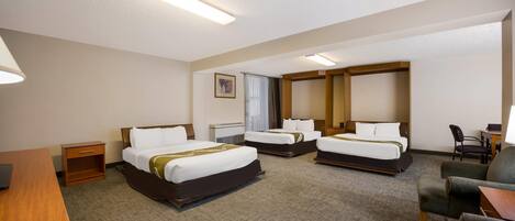 Quarto de hotel com três camas, uma escrivaninha, uma cadeira e uma pequena mesa.
