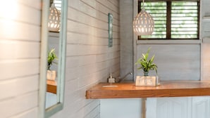 A bathroom with a wooden vanity, two white stools, a mirror, and two hanging pendant lights. - ECO Lifestyle & Lodge (Bathsheba)