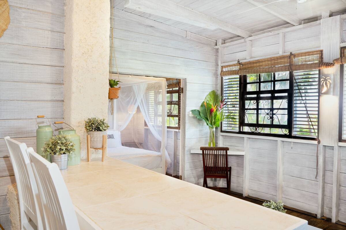 A room with a bed, a dining table, and a window with shutters.