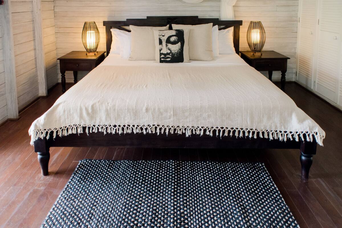 A large bed with a white bedspread, two nightstands with lamps, a patterned rug, and wooden walls.