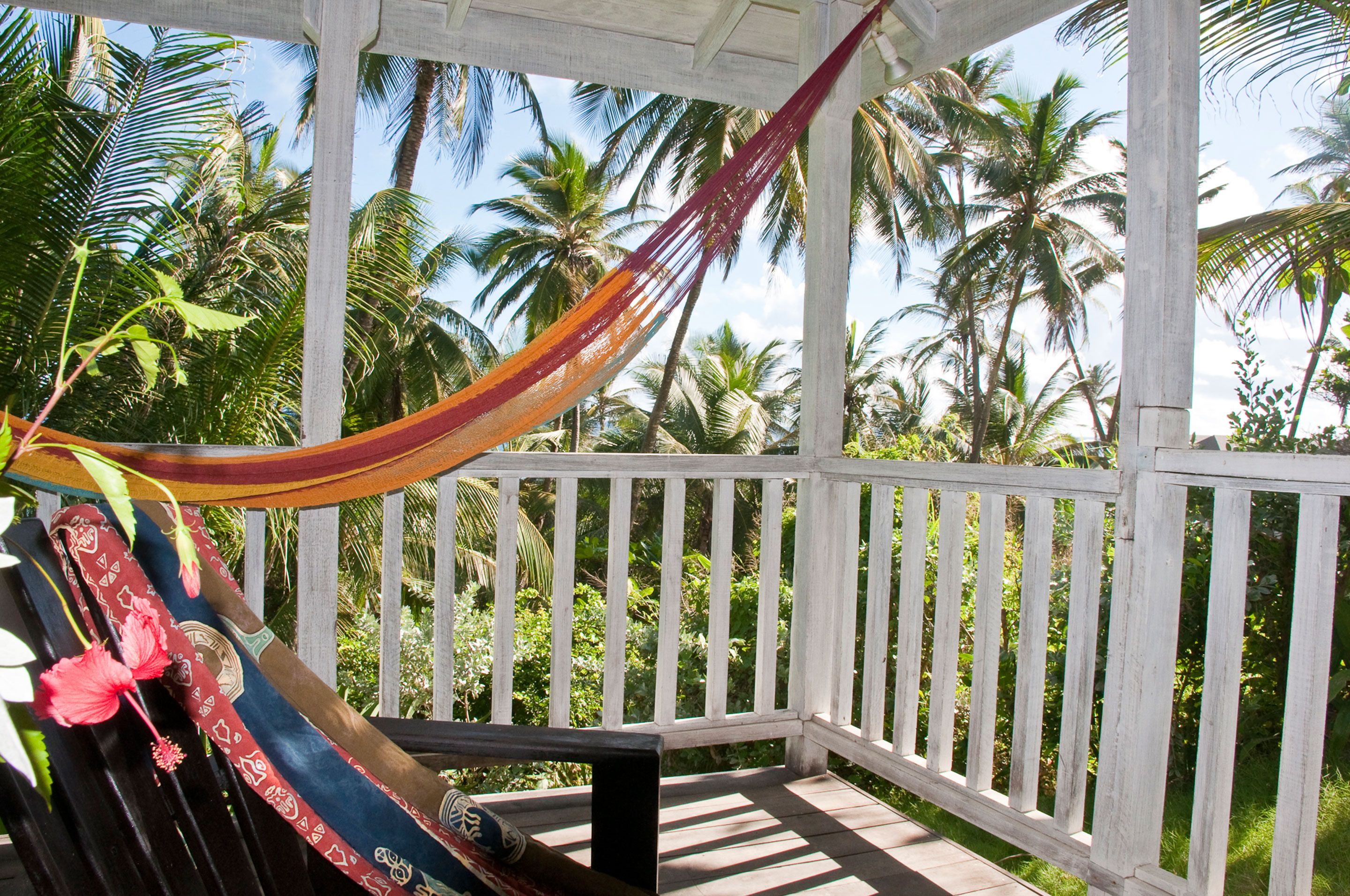 A hammock on a wooden deck with a view of palm trees.