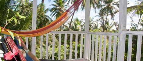 A hammock on a wooden deck with a view of palm trees.