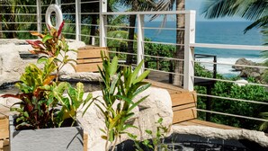A wooden deck with a white railing overlooking a body of water, surrounded by greenery and palm trees. - ECO Lifestyle & Lodge (Bathsheba)
