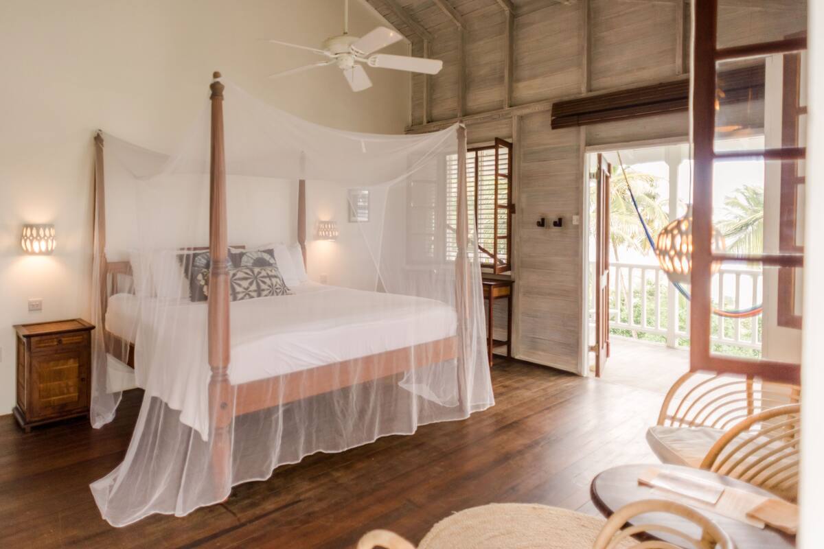 A four-poster bed with a canopy, a ceiling fan, and a view of the outdoor area through a door.