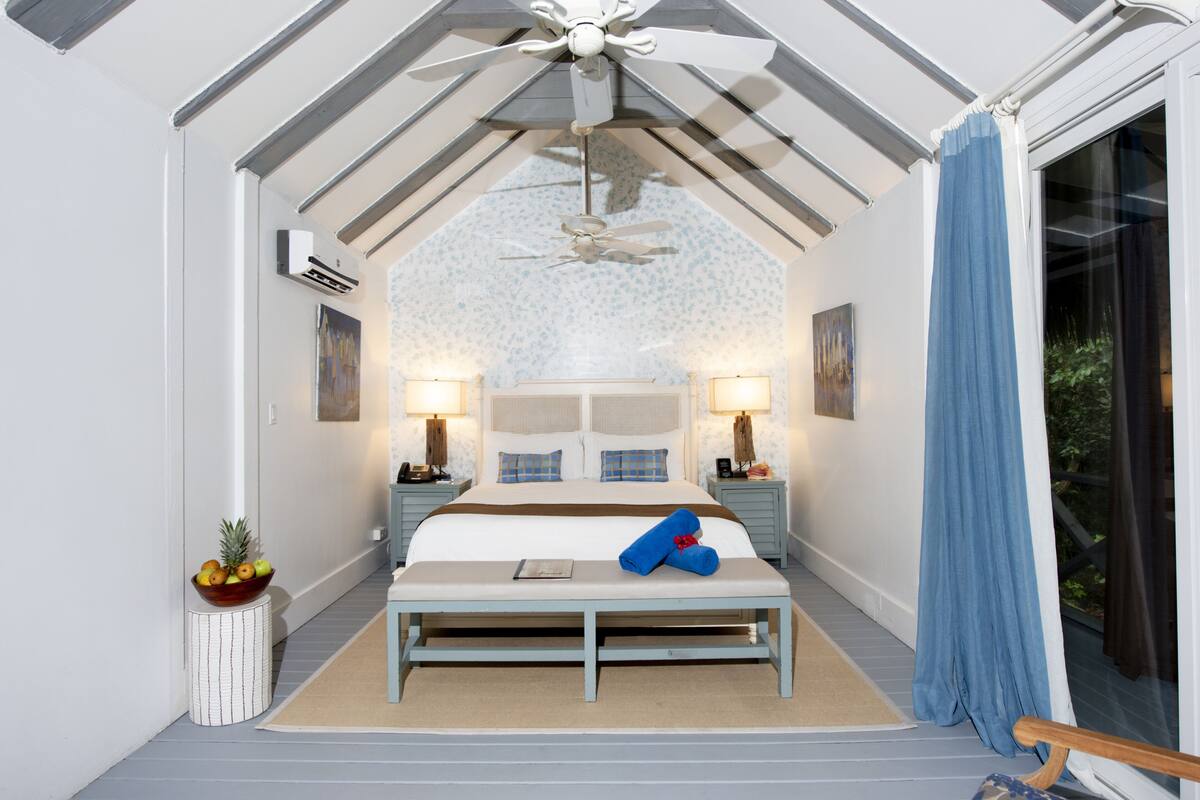 A bedroom with a bed, bedside tables, a ceiling fan, and a view through a window.