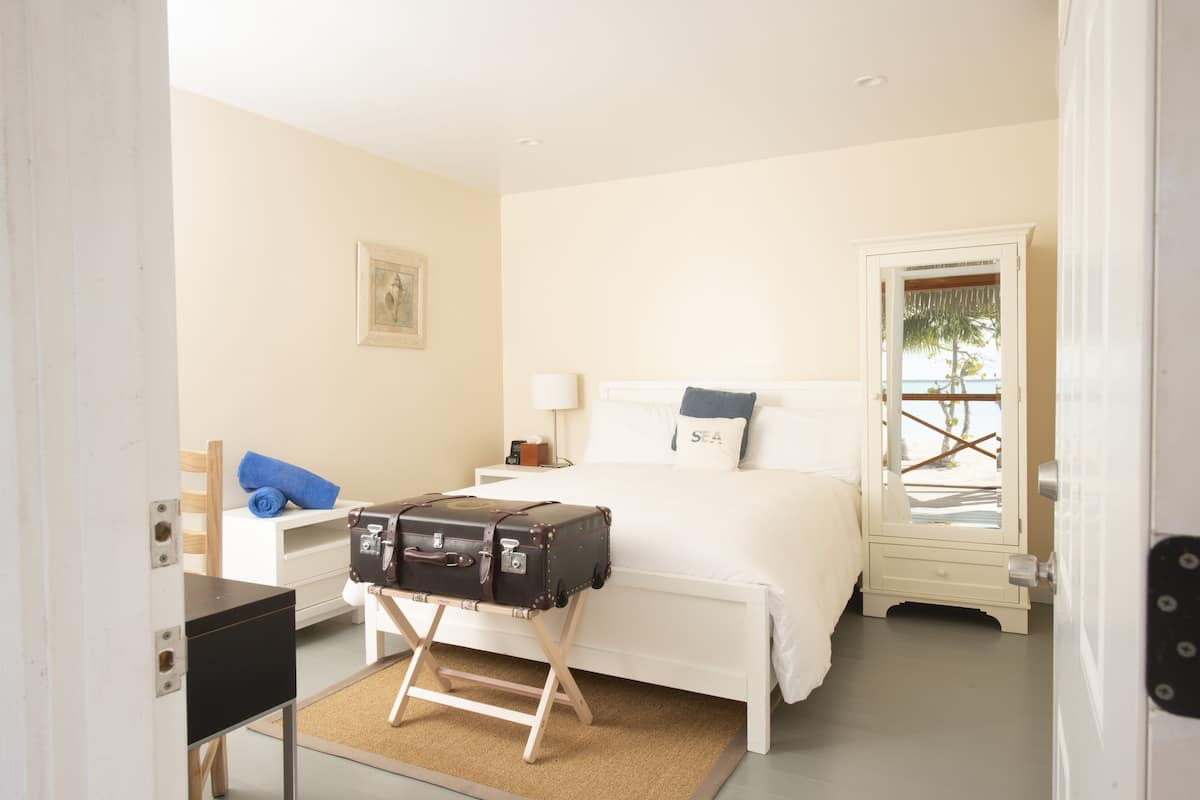 A bedroom with a bed, a suitcase, a nightstand, a lamp, and a door with a view.