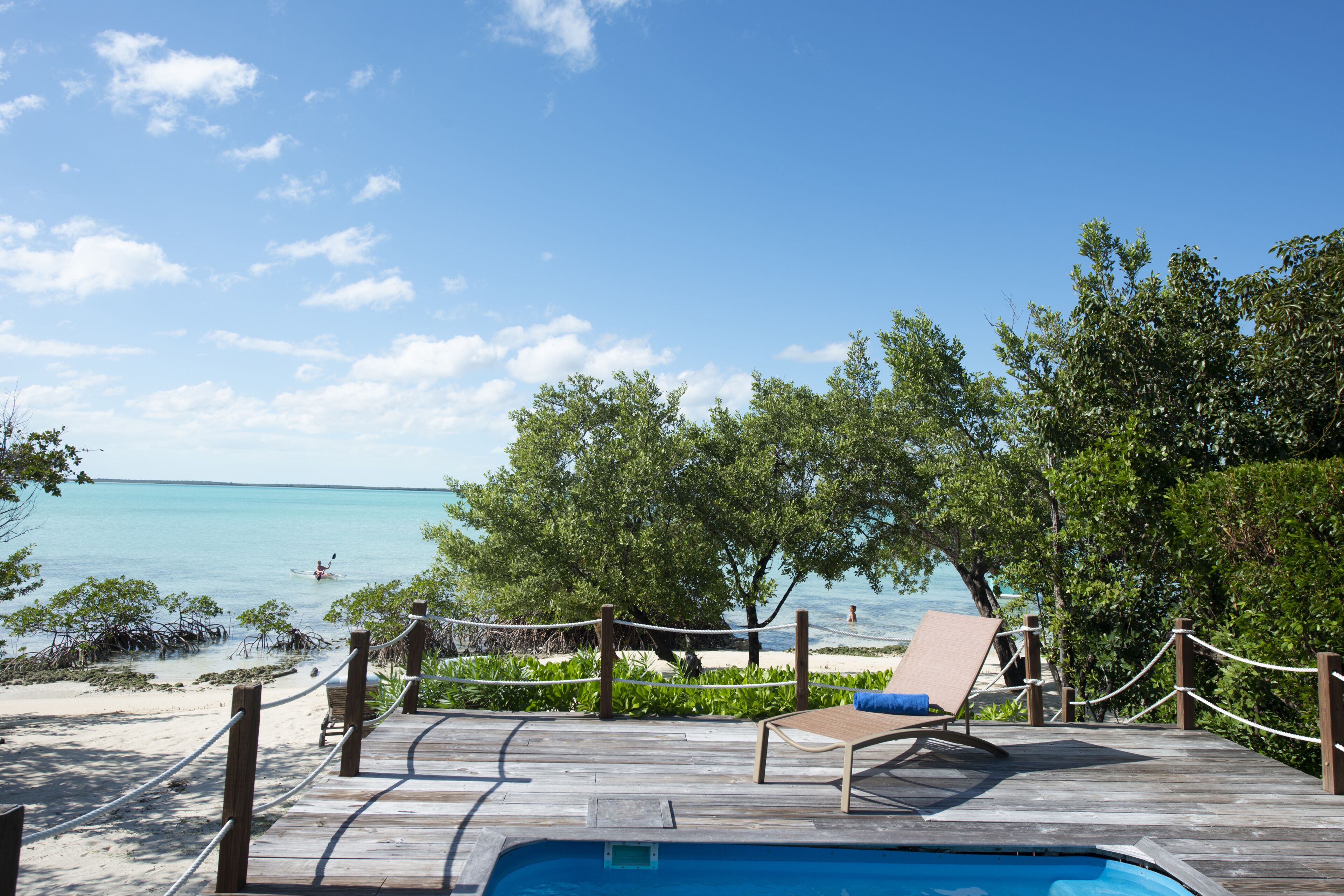 A wooden deck with a pool, lounge chairs, and a view of the ocean.