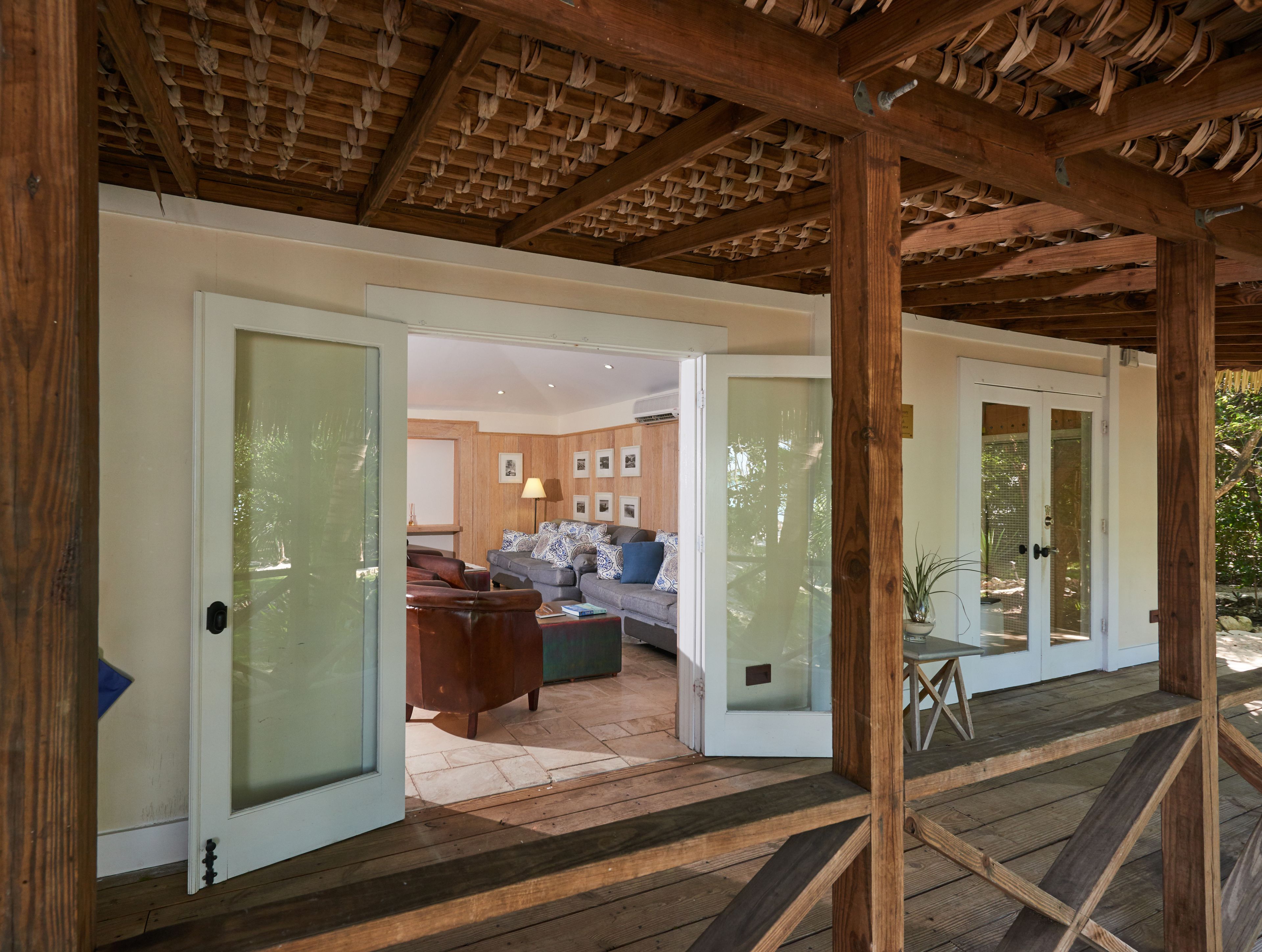 A wooden deck with a glass door leading to a living area with a sofa, a coffee table, and a lamp.