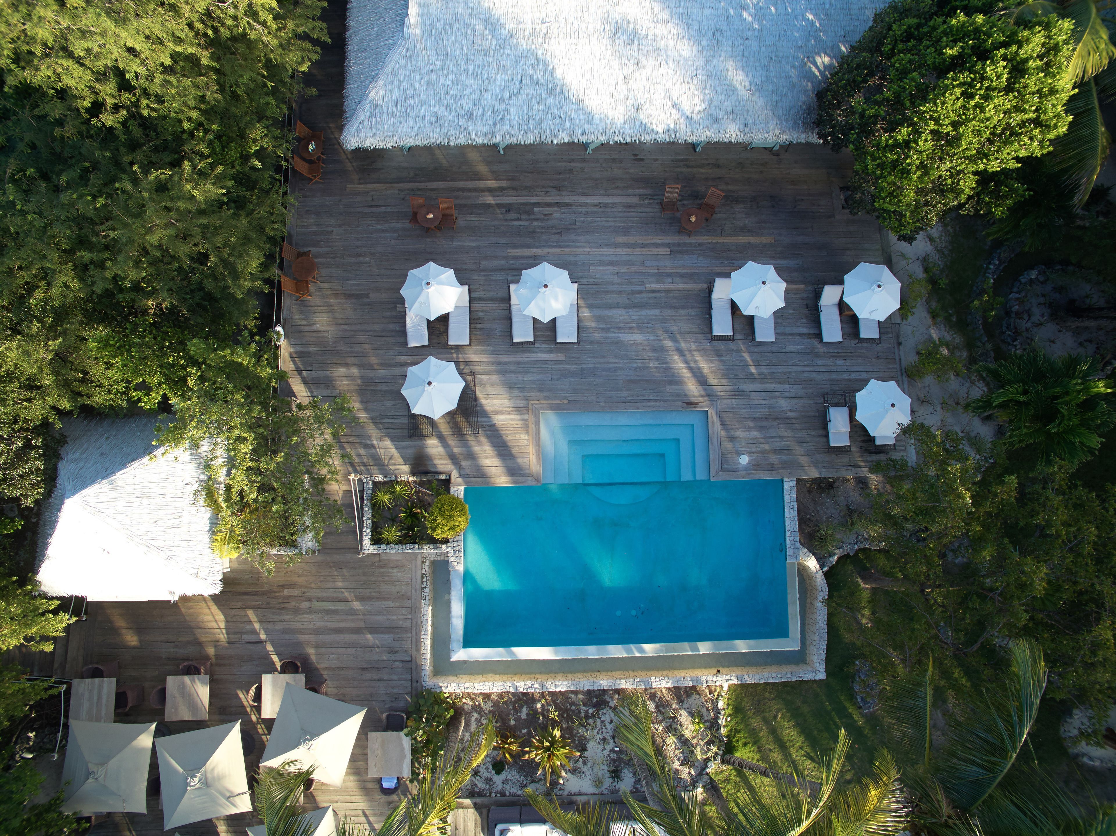 An aerial view of a wooden deck with a swimming pool, surrounded by lounge chairs and umbrellas.