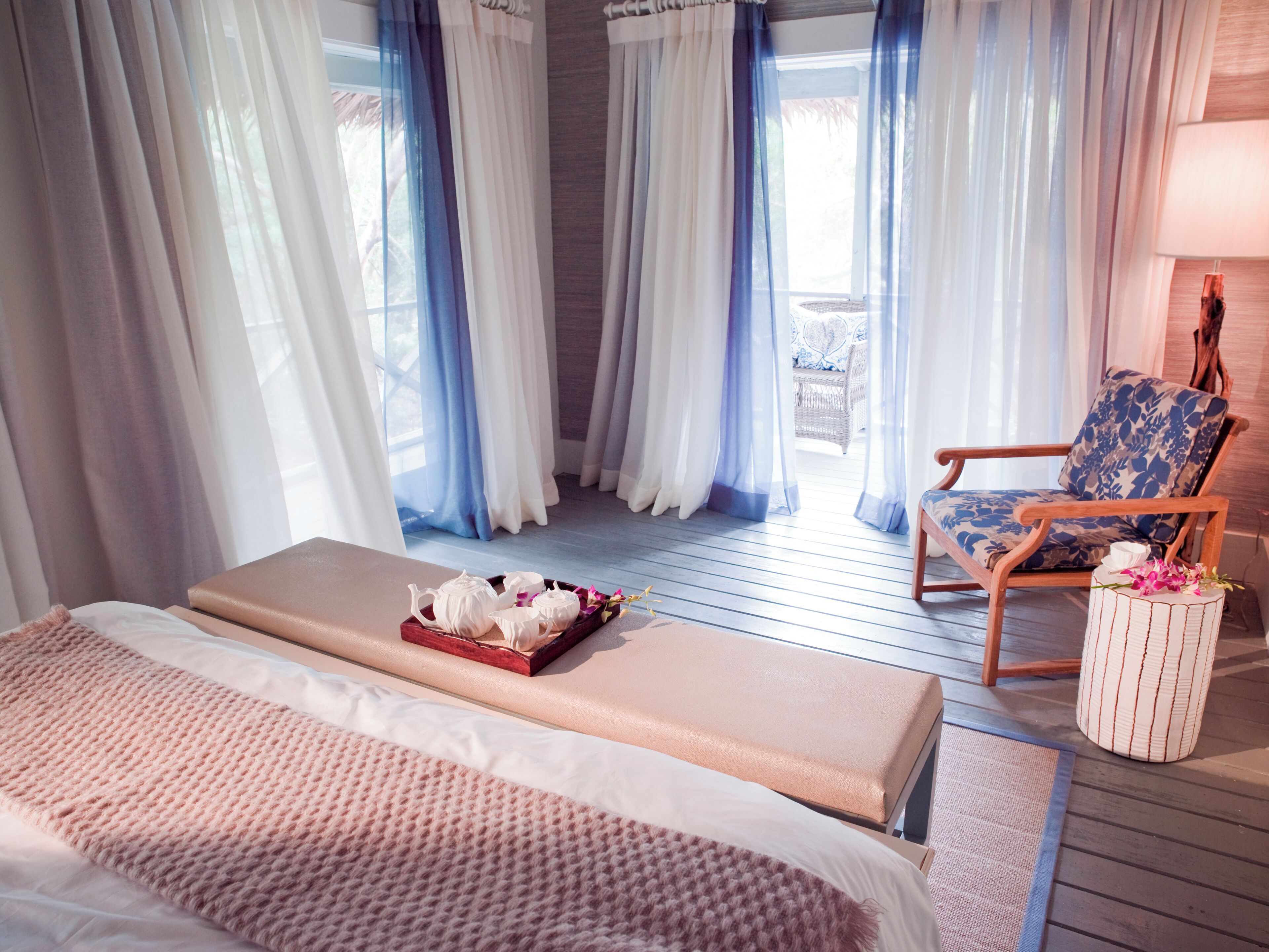 A bedroom with a bed, a bench, a chair, and a small table with a tray of items.