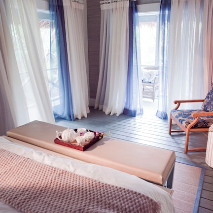 A bedroom with a bed, a bench, a chair, and a small table with a tray of items.