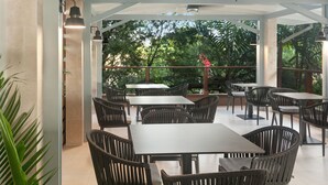 An outdoor patio area with tables and chairs, a ceiling fan, and a view of trees. - Cara Hotels Trinidad (Claxton Bay)